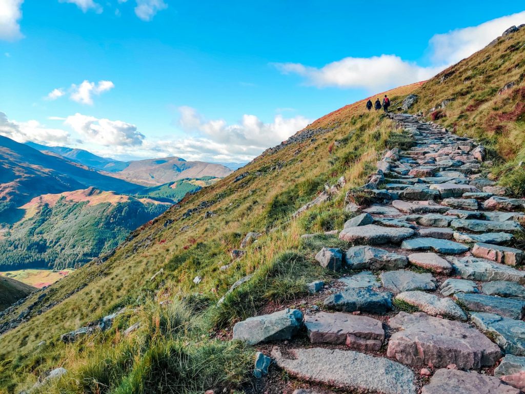 gray rocky pathway on green grass field near mountains under blue sky during daytime